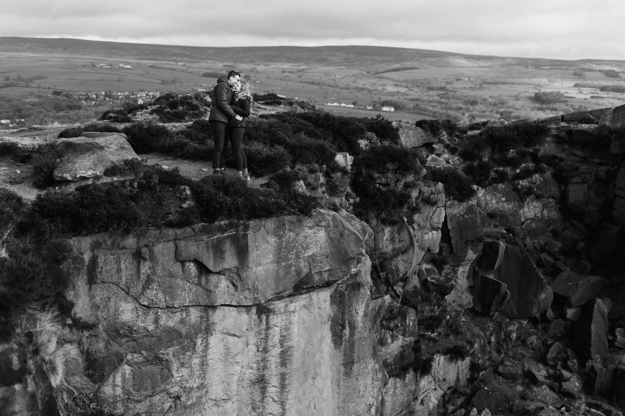 A couple posing for a photo stood on a cliff edge with the moors in the background